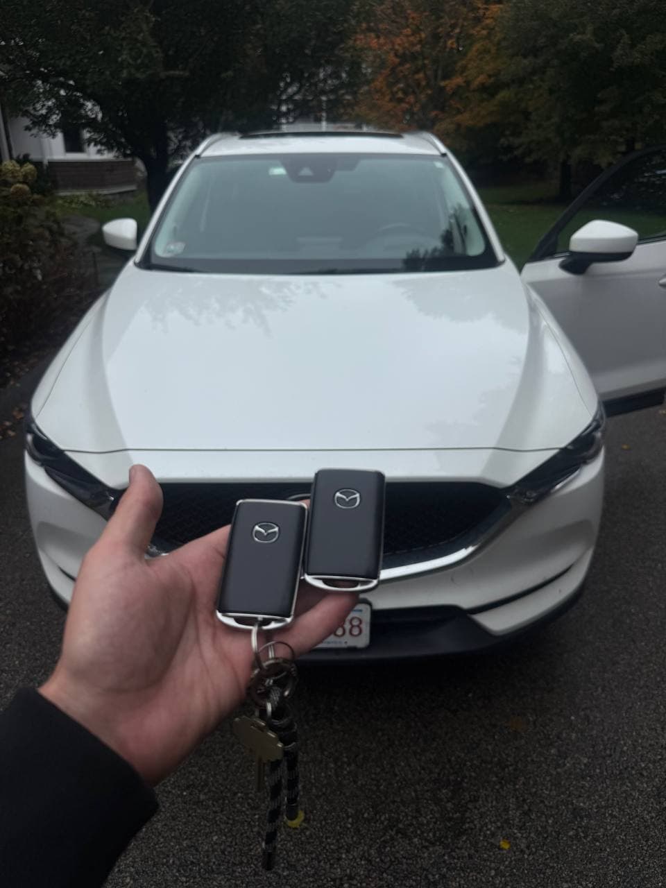 Hand holding two black Mazda key fobs in front of a white Mazda SUV.