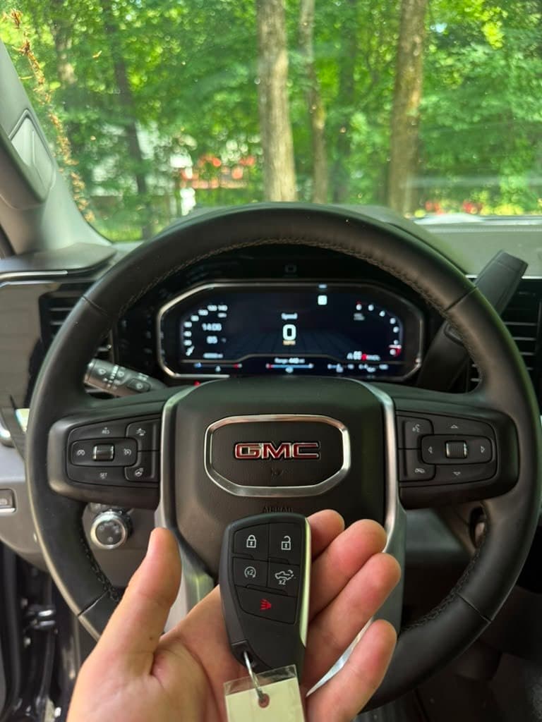 Hand holding a GMC key fob in front of a steering wheel and digital dashboard.